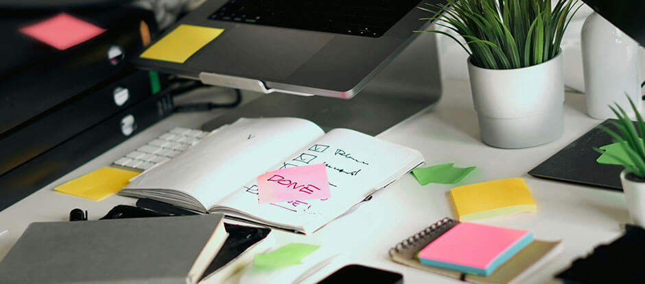 A cluttered desk with post it notes and checklists