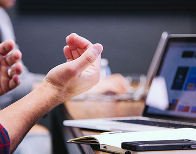 Hands gesturing with a laptop and notepad on the desk